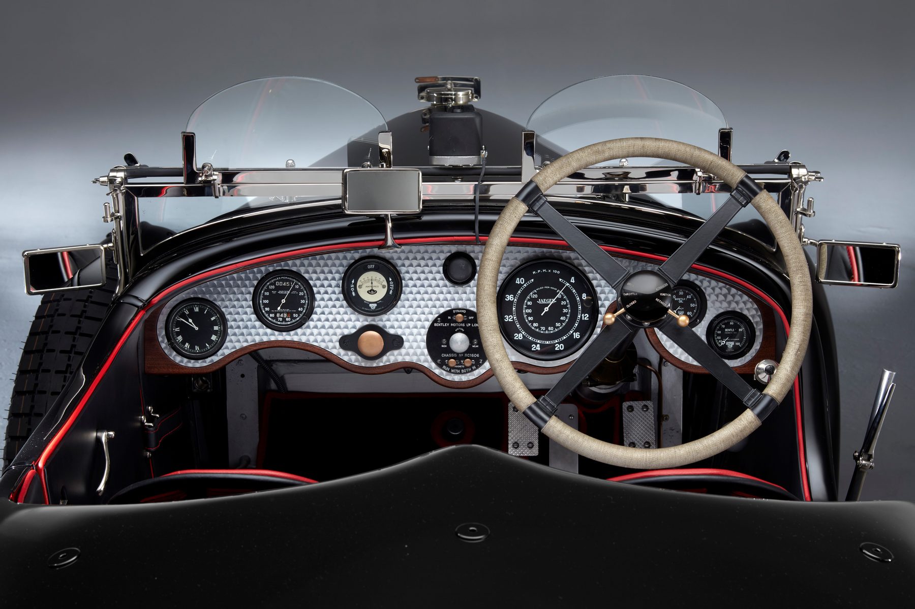 Engine-turned dashboard with fighter-aircraft array of dials, red piping and cord-bound steering wheel